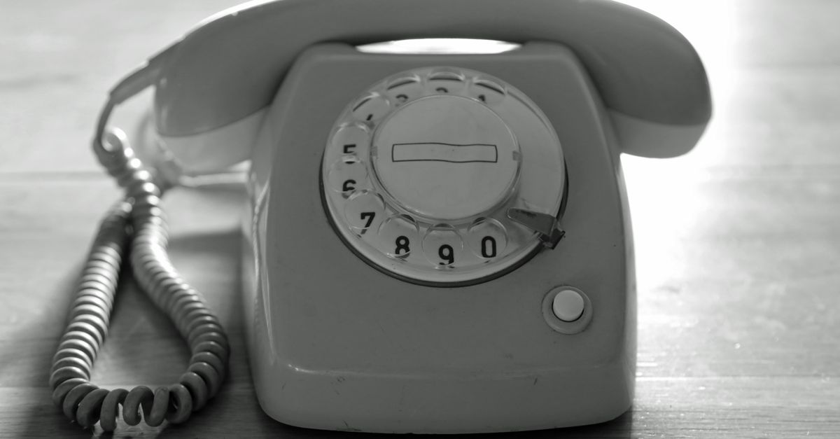 High contrast black and white image of a vintage rotary phone on a wooden surface emphasizing nostalgic communication.